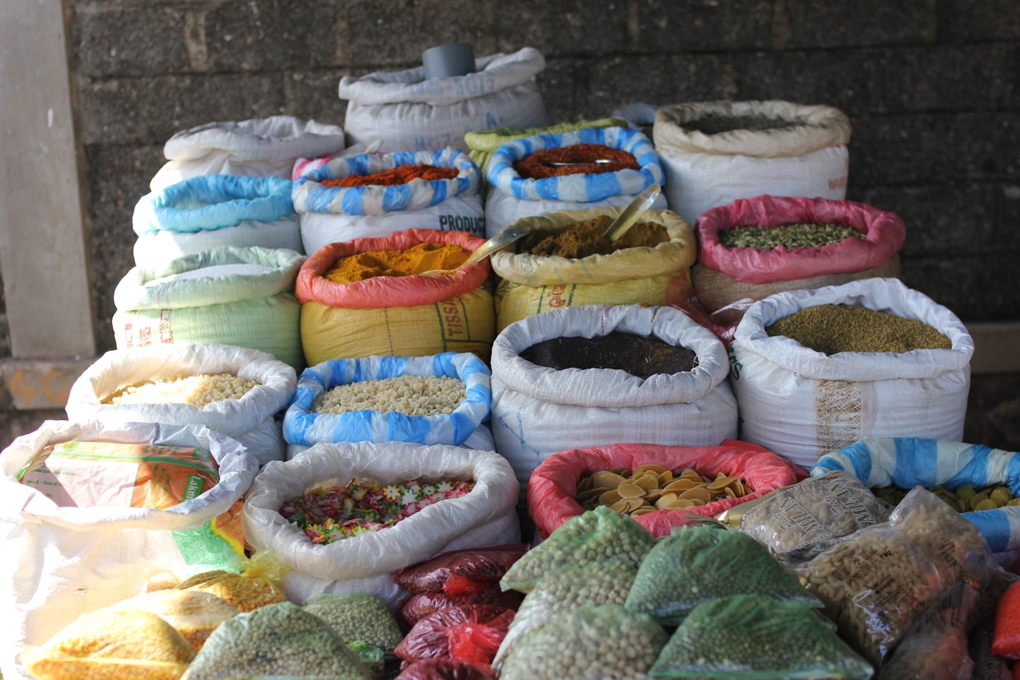 Colorful spices and grains displayed in open sacks and clear bags.
