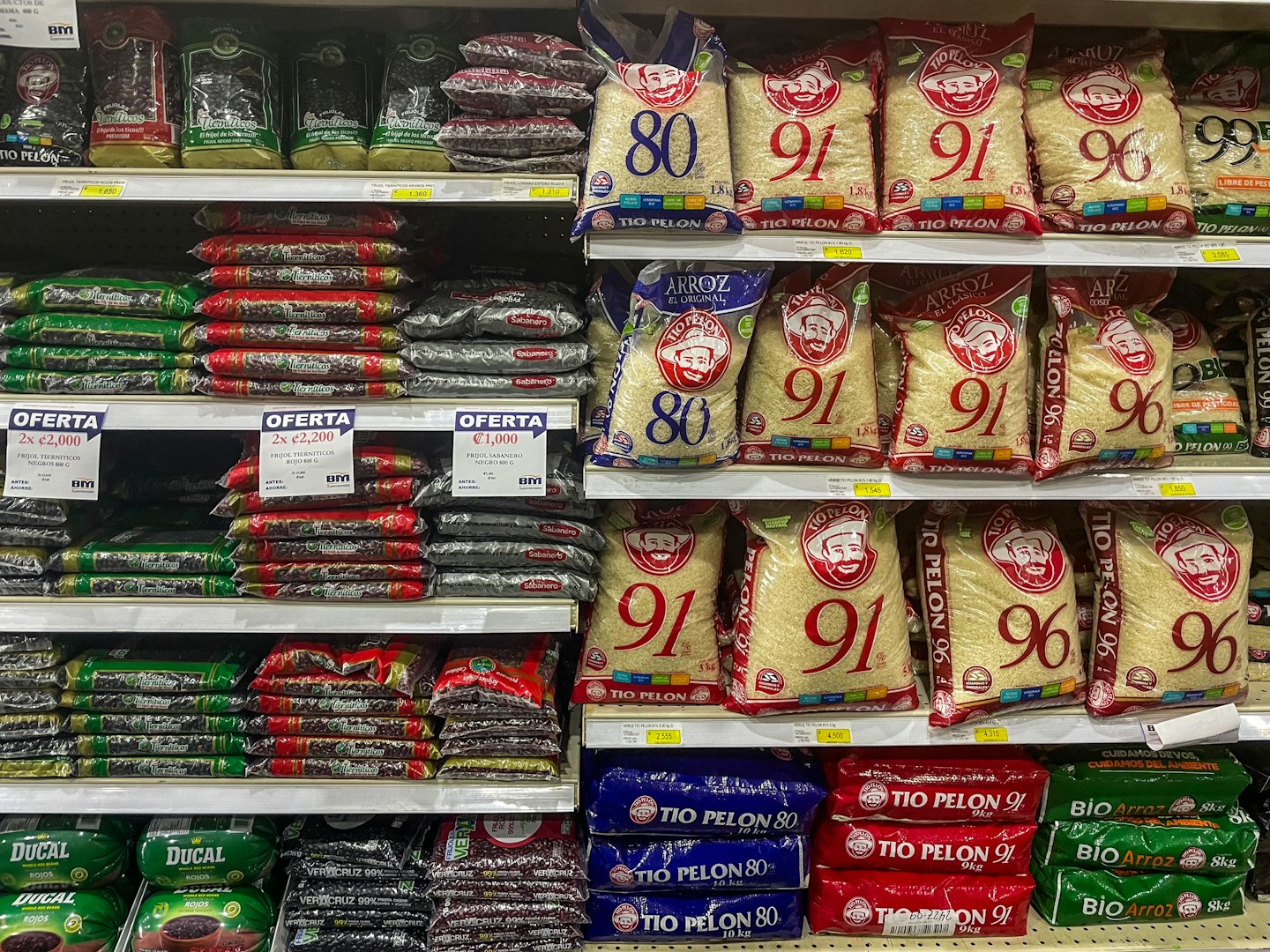 Shelves stocked with bags of rice and beans in a supermarket.