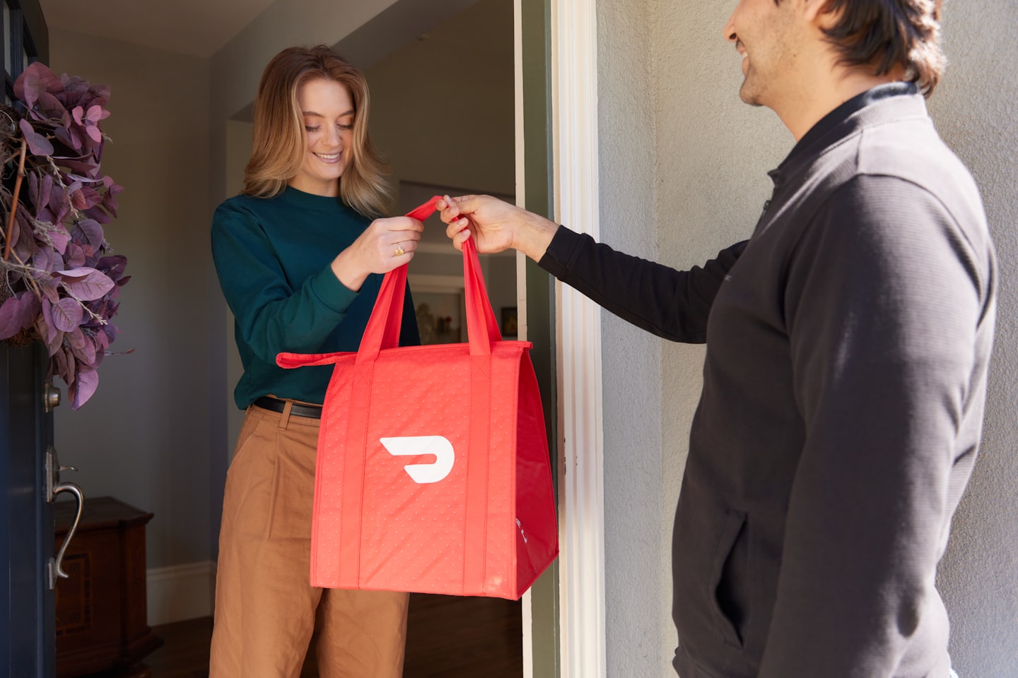 Customer smiling while accepting a delivery bag at her door.