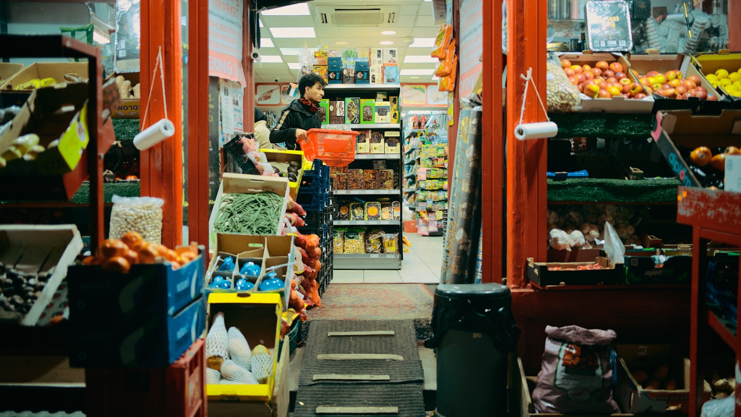 Man with red basket shops in a busy grocery store aisle.